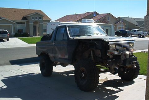 1986 Ford Bronco - This heavily modified Ford Bronco, likely from the early 1980s, sits in a suburban driveway with its front end partially disassembled.