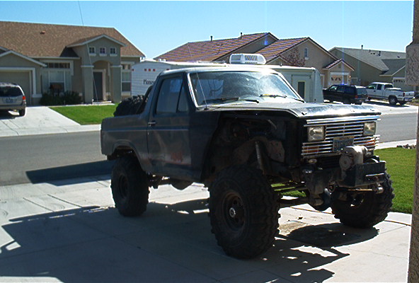 Modified Ford Bronco with large tires and a winch on the front bumper, parked in a driveway