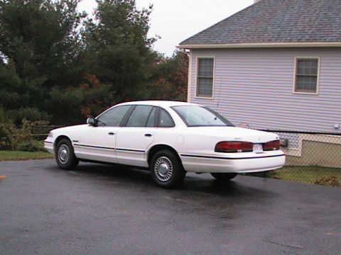 1995 Ford Crown Victoria - A white 1995 Ford Crown Victoria is parked on a wet driveway next to a house.