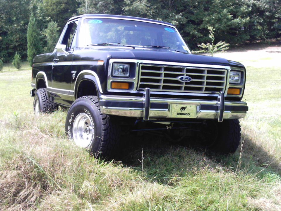 Black 1980s Ford Bronco 4x4 with chrome grille guard in a grassy field