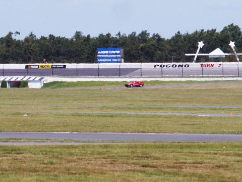 2001 Mercury Grand Marquis - A red sports car navigates the track at Pocono Raceway, with sponsor signage visible on the retaining wall.