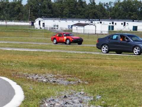 2001 Mercury Grand Marquis - Two cars are on a race track with buildings in the background.
