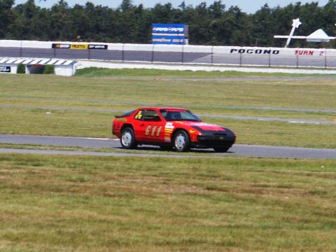2001 Mercury Grand Marquis - A red sports car with racing decals drives on a track with grandstands in the background.