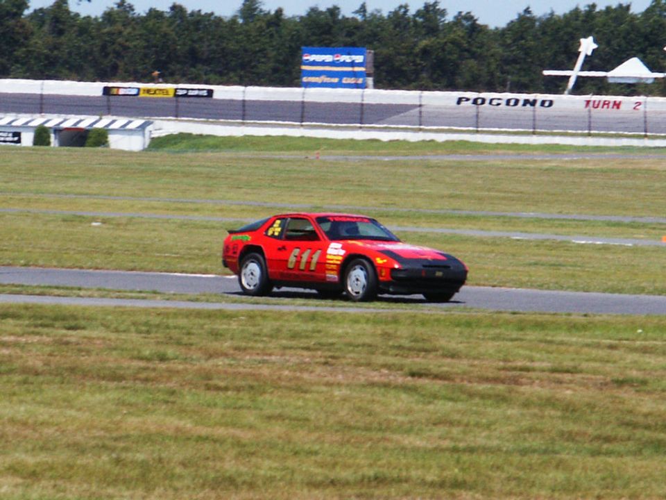 Red sports car with black hood and racing numbers 611 on the side, on a race track
