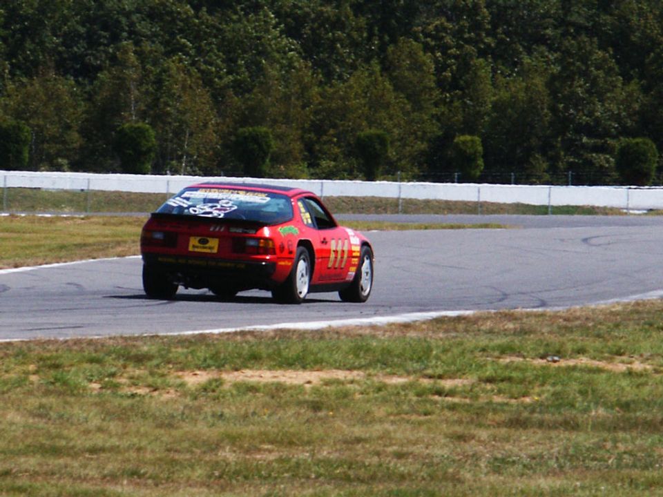 Red race car with number 111 on the side, driving on a track with trees in the background