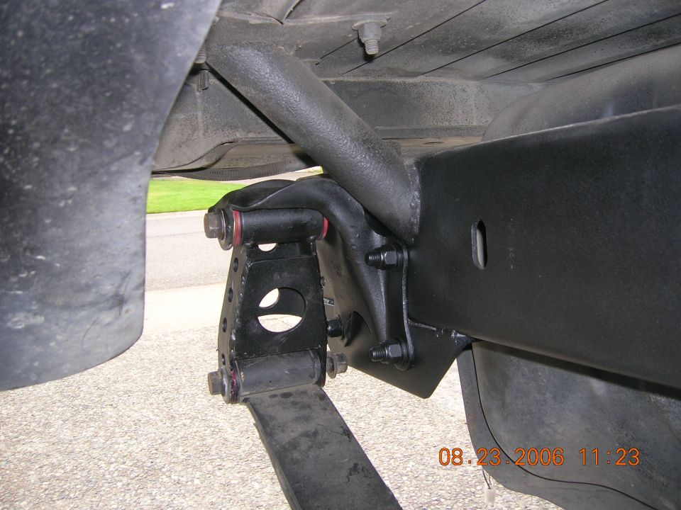 Underside close-up of black leaf-spring shackle, mount, and bolts on a vehicle frame