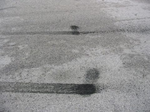 1985 Ford Crown Victoria LTD - Tire marks and dark fluid stains are visible on the asphalt surface.