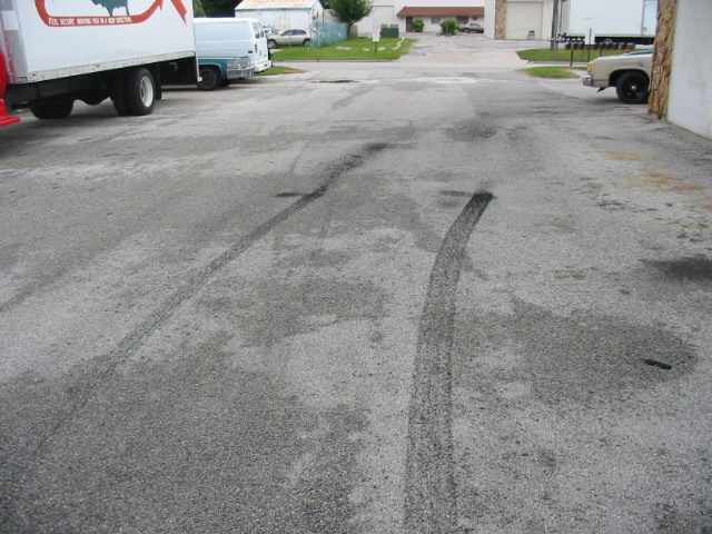 Tire marks on wet asphalt with a white truck and van in the background