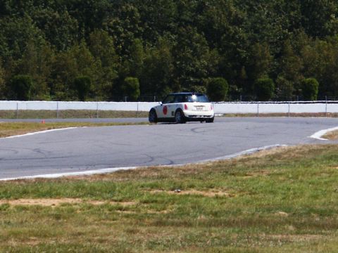 2001 Mercury Grand Marquis - A white Mini Cooper navigates a turn on a paved race track with trees in the background.