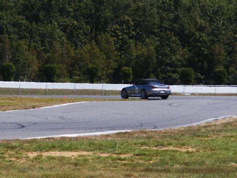 2001 Mercury Grand Marquis - A silver convertible sports car navigates a turn on a race track, with trees and a white barrier in the background.