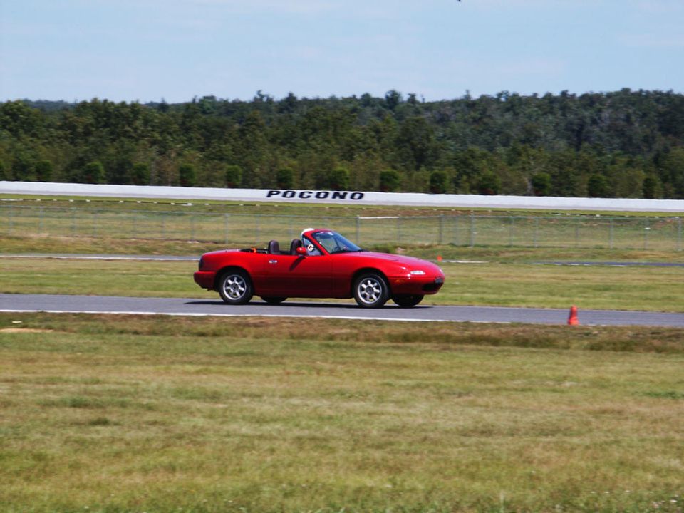 Red convertible sports car on a paved track with grassy infield and trees in background