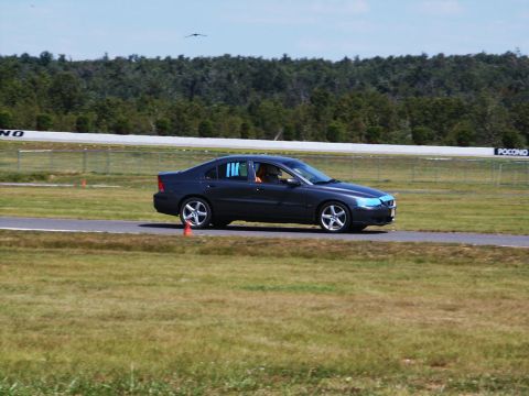 2001 Mercury Grand Marquis - A dark sedan drives on a race track with trees and a fence in the background under a clear sky.