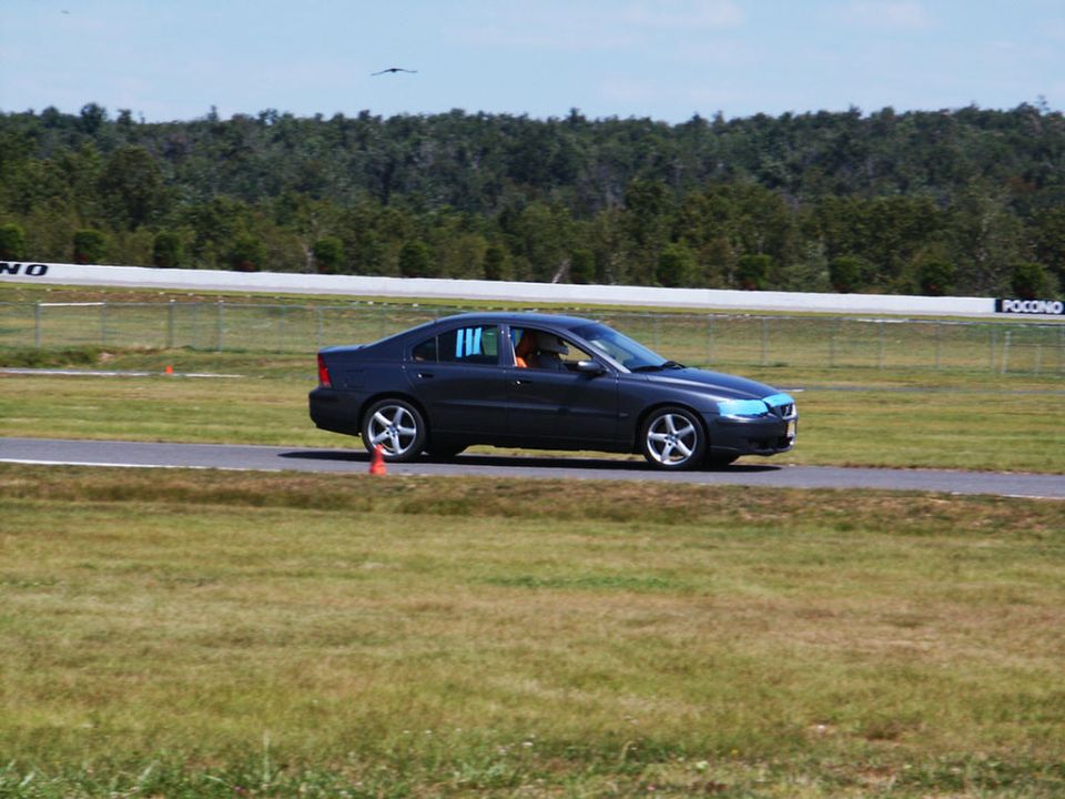 dark sedan with blue headlight covers on a race track, orange cones on the side