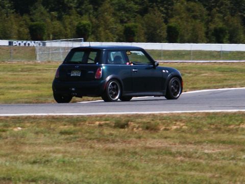2001 Mercury Grand Marquis - A Mini Cooper drives on a race track with a wooded area and fence in the background.