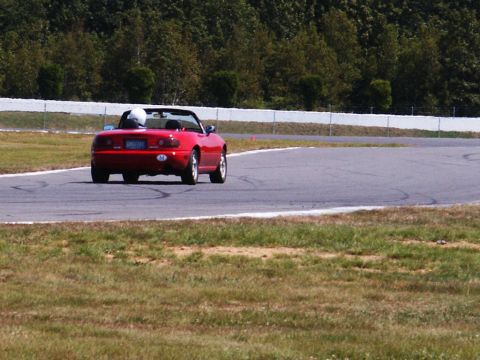 2001 Mercury Grand Marquis - Red convertible sports car navigates a turn on a race track with trees in the background.