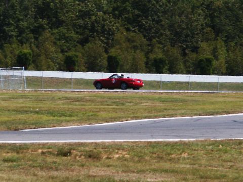 2001 Mercury Grand Marquis - A red convertible sports car is seen on a race track with trees in the background.