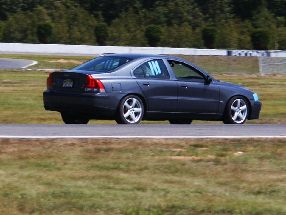 Dark gray Volvo S60 on race track, side view. Blue window netting visible