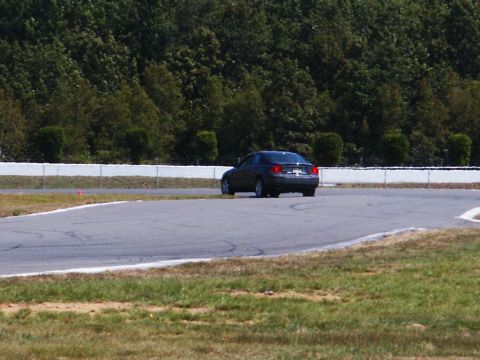 2001 Mercury Grand Marquis - A dark sedan navigates a turn on a paved race track with a wooded area and safety barrier visible.