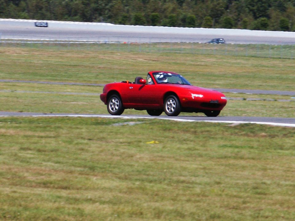 Red convertible sports car driving on a race track with a driver wearing a helmet