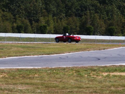 2001 Mercury Grand Marquis - A red convertible sports car navigates a turn on a race track with trees and a white fence in the background.