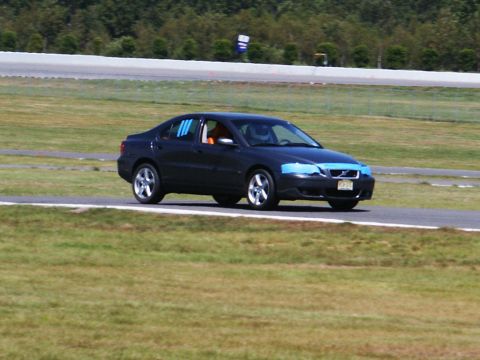 2001 Mercury Grand Marquis - A dark sedan is captured on a race track, with blue tape applied to its front end and blue stripes visible on the driver's side window.