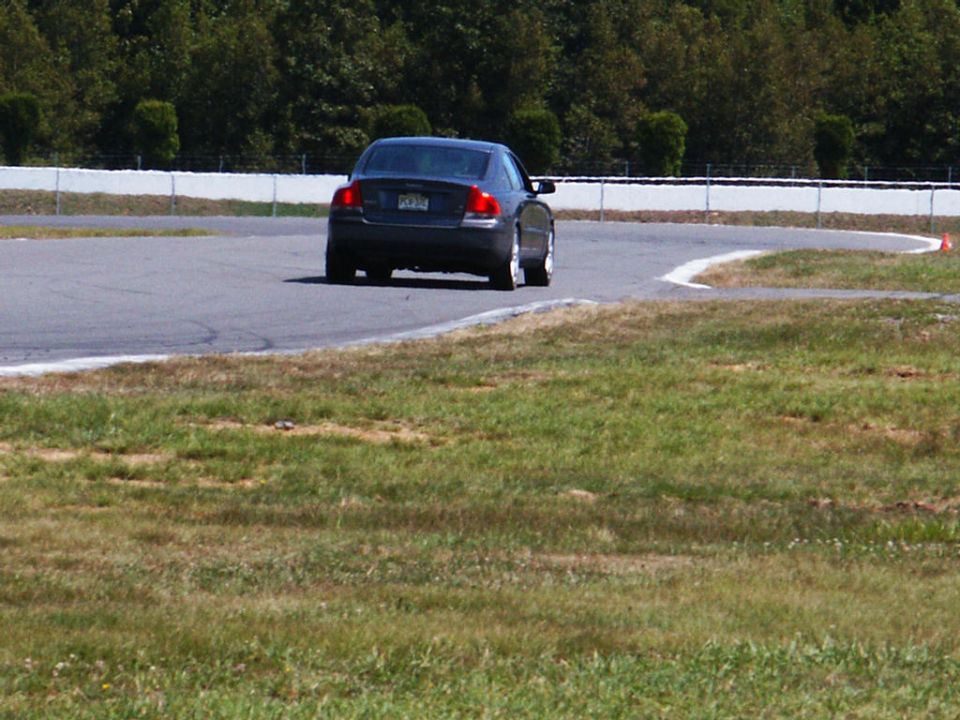 Dark sedan on race track, rear view. Watermark: SUPERMOTORS www.supermotors.net