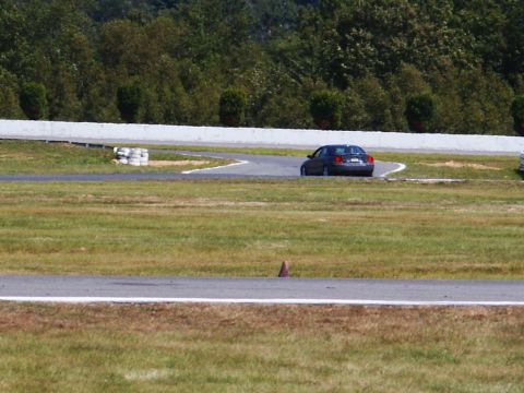 2001 Mercury Grand Marquis - A dark sedan navigates a turn on a race track with grassy verges and a white barrier.