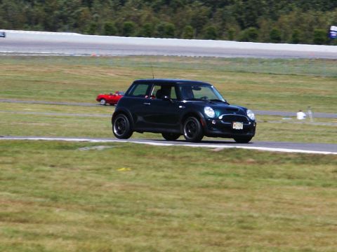 2001 Mercury Grand Marquis - A dark green Mini Cooper drives on a race track, with a red convertible visible in the distance.