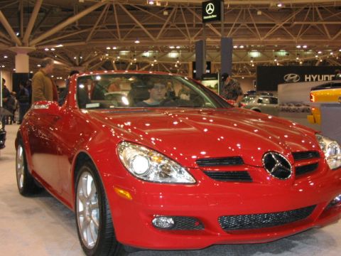 1994 Mazda 626 - A red convertible is displayed at an auto show with a Mercedes-Benz logo visible.