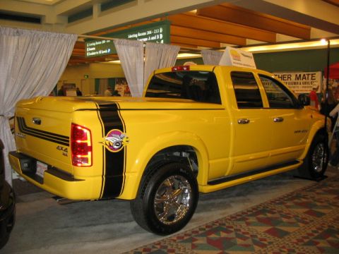 1994 Mazda 626 - Yellow Dodge Ram pickup truck with custom racing stripes and bee graphic displayed indoors.