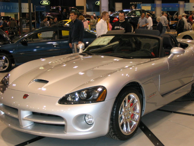 Silver convertible Dodge Viper SRT-10 with red brake calipers. Other cars and people in background