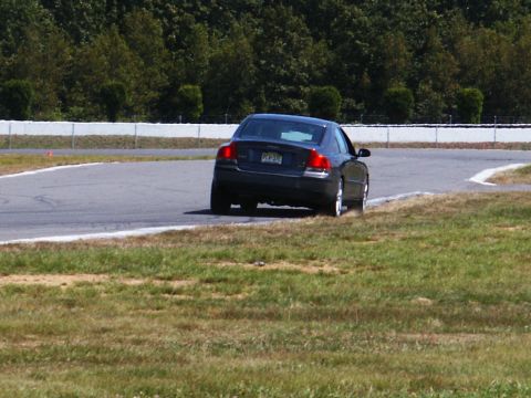 2001 Mercury Grand Marquis - A dark sedan navigates a turn on a race track with grassy shoulders.