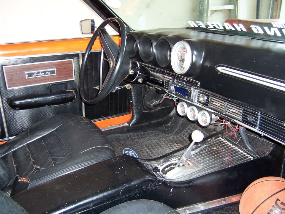 Black interior of a classic Ford with Fairlane 500 badge, tach and floor shifter