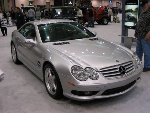 1994 Mazda 626 - A silver Mercedes-Benz SL-Class is displayed at an auto show, with other vehicles and attendees visible.