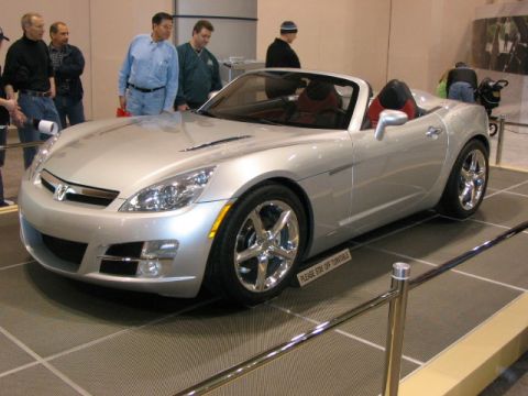 1994 Mazda 626 - A silver convertible sports car is displayed at an auto show with onlookers.