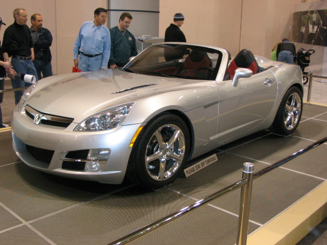 Silver convertible sports car with red interior, chrome wheels, and a badge on the grille