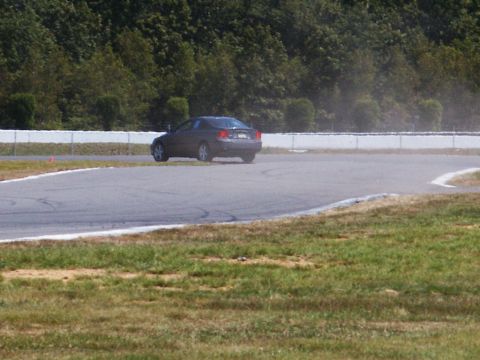 2001 Mercury Grand Marquis - A dark sedan navigates a turn on a paved race track with trees and a fence in the background.