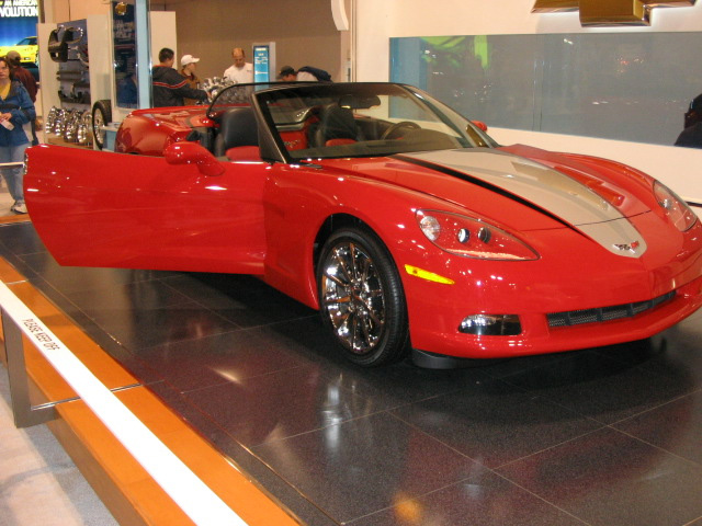 Red convertible sports car with driver's door open, silver stripe on hood