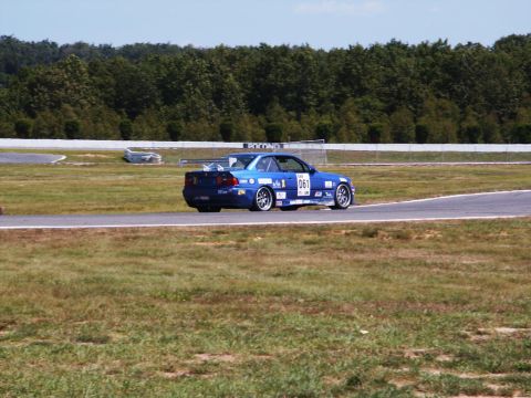 2001 Mercury Grand Marquis - A blue race car navigates a turn on a sunny day at the track.