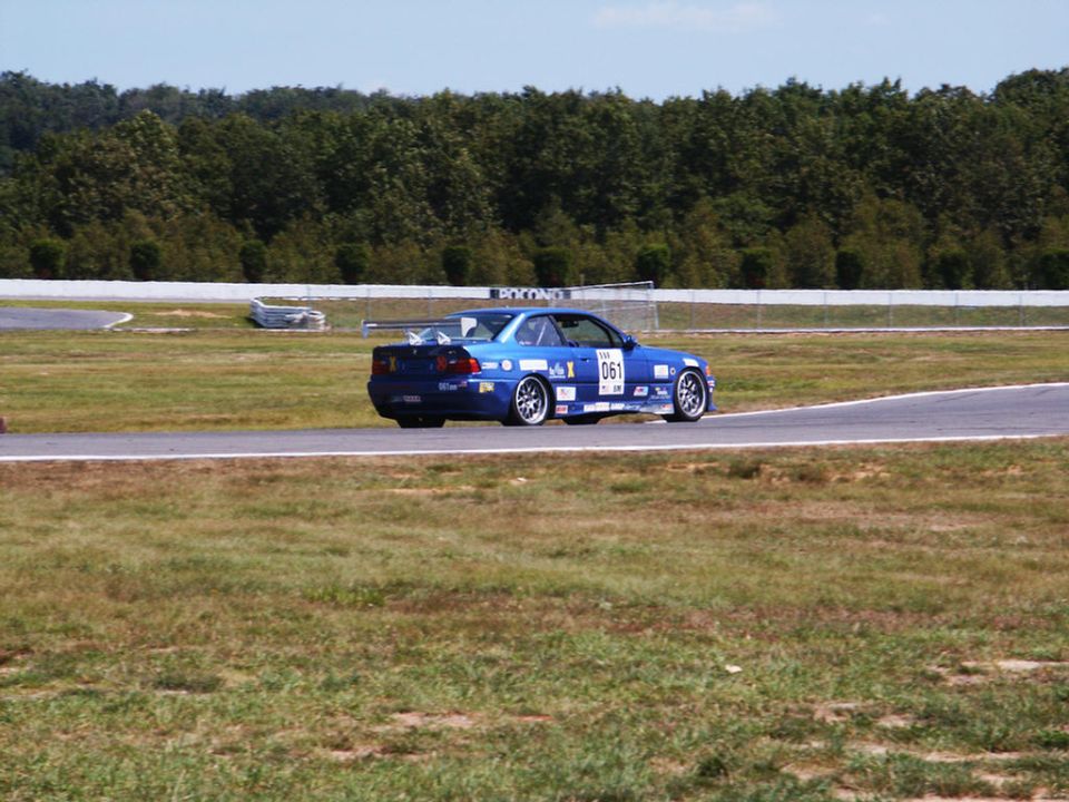 Blue race car with number 061 on the side, driving on a track with trees in the background