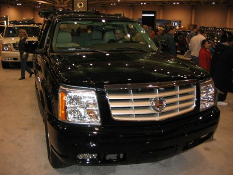 1994 Mazda 626 - A black Cadillac Escalade is displayed at an auto show with other vehicles in the background.