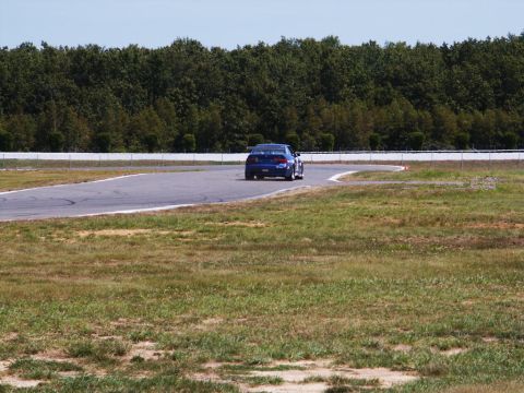 2001 Mercury Grand Marquis - A blue sedan navigates a turn on a race track, with trees lining the background.