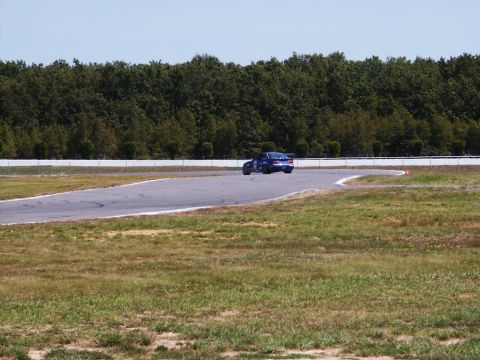2001 Mercury Grand Marquis - A blue sedan navigates a turn on a race track, with trees and a fence in the background.