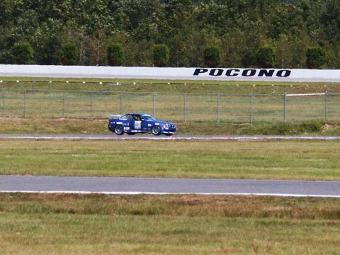 2001 Mercury Grand Marquis - A blue race car speeds around a track, with the 'POCONO' sign visible in the background.