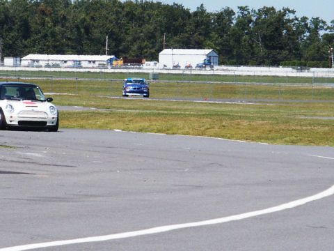 2001 Mercury Grand Marquis - Two cars are on a racetrack with trees and buildings in the background.