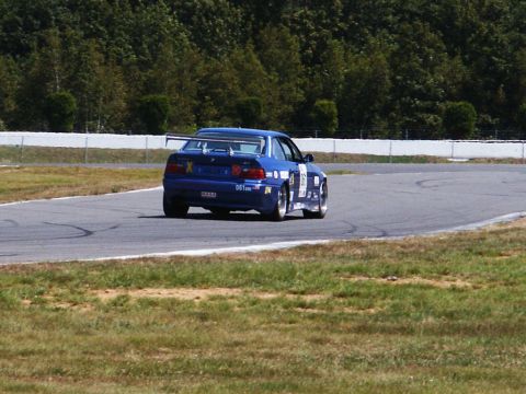 2001 Mercury Grand Marquis - A blue race car navigates a turn on a sunny day at the track.