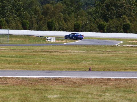2001 Mercury Grand Marquis - A blue race car navigates a turn on a paved track surrounded by grass and trees.