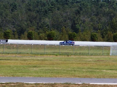 2001 Mercury Grand Marquis - A blue sedan is seen on the race track with a fence in the foreground and trees behind the track.