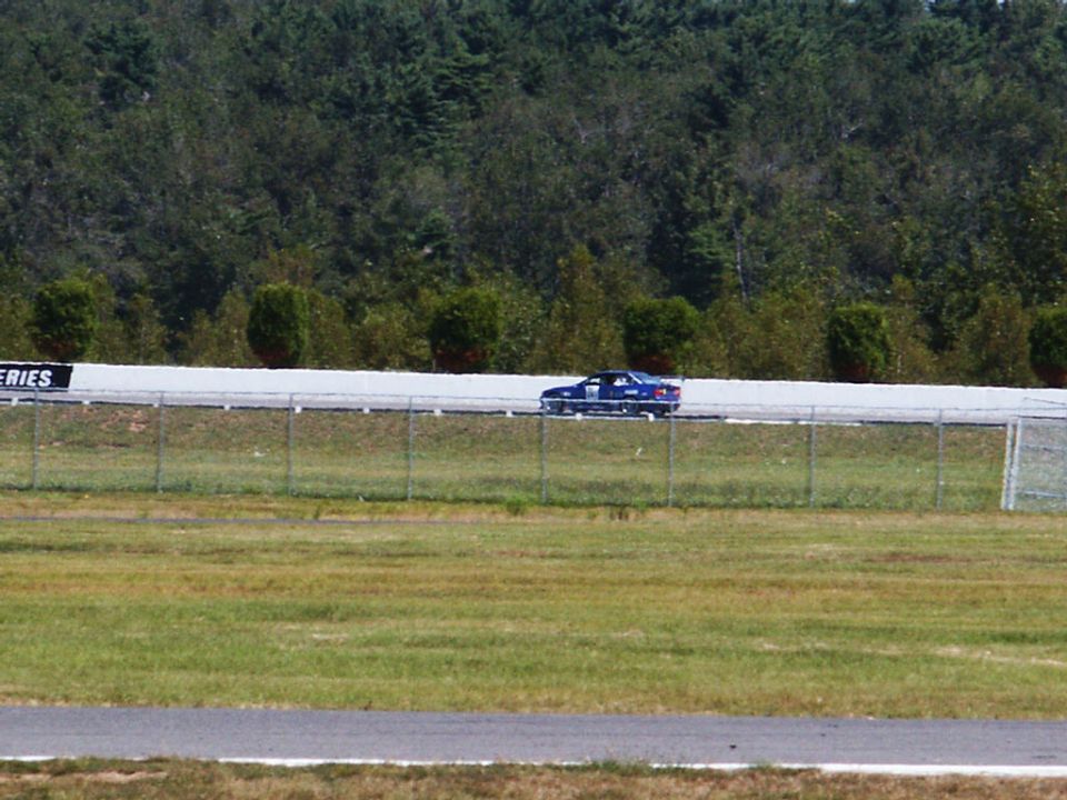 blue sedan driving on a race track with trees in the background