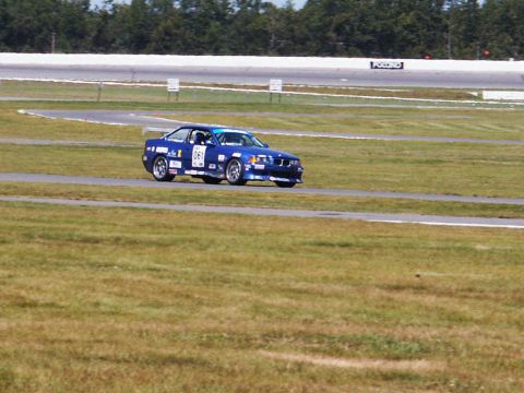 2001 Mercury Grand Marquis - A blue race car navigates a turn on a grassy racetrack.